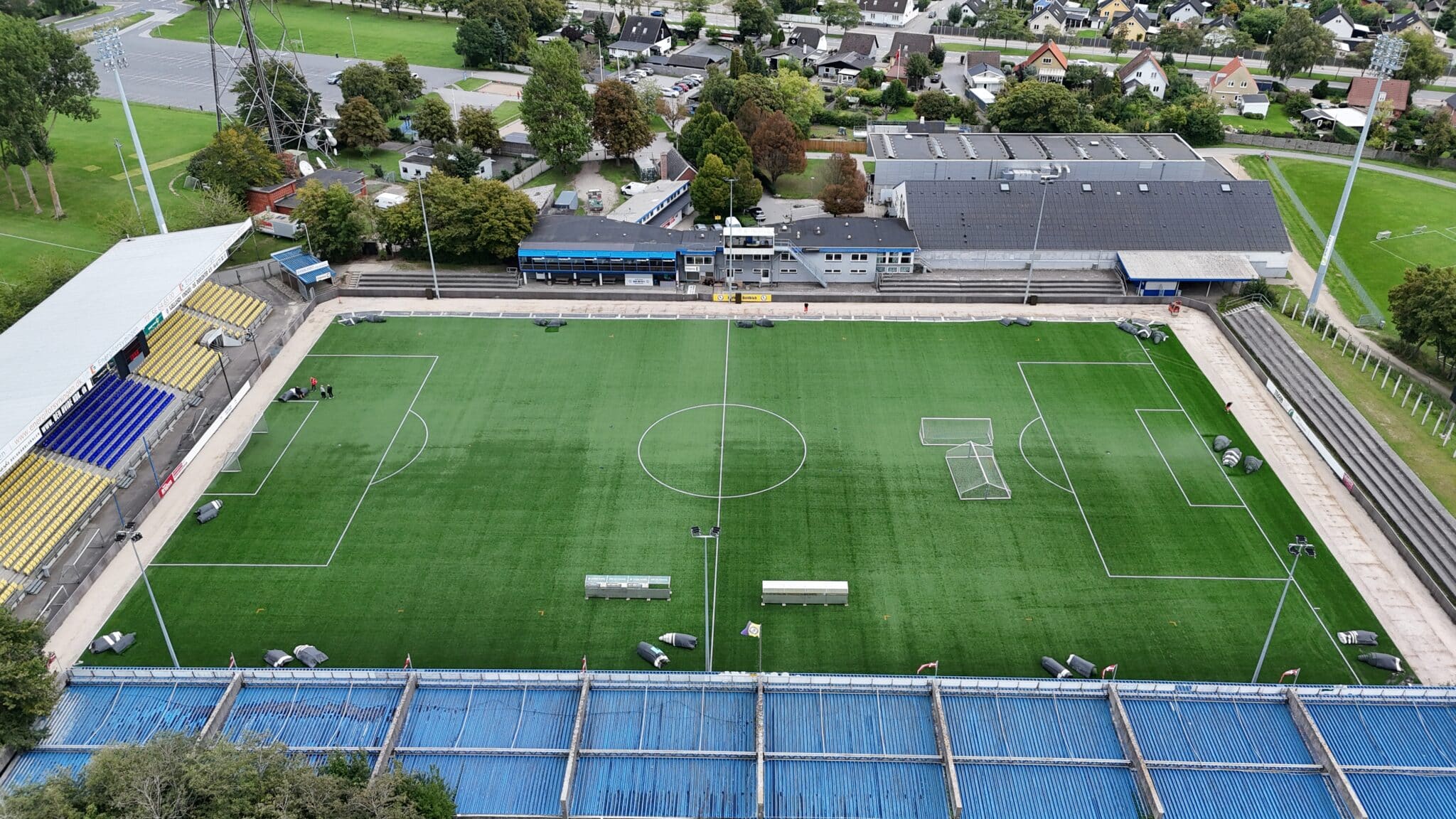 Airfoto af en fodboldbane med kunstgræs og tribuner.